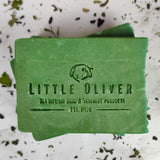 A green bar of handmade green tea soap surrounded by green tea leaves on a white marble background