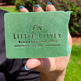 A female hand holding up a bar of Green Tea Soap. Stamped with Little Oliver Tea Infused Bath and Skincare Products logo